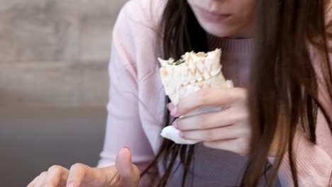 Mujer-irreconocible-comer-danar-o-Shawarma-sentado-en-un-café-y-escribiendo-un-mensaje-en-el-teléfono-móvil.