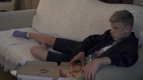 Young-man-eats-pizza-laying-at-sofa