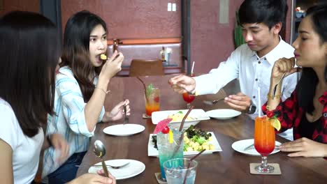 Grupo-de-cuatro-jóvenes-asiáticos,-un-hombre,-tres-mujeres,-comiendo-y-hablando-en-la-cafetería-y-restaurante.-Concepto-de-la-amistad