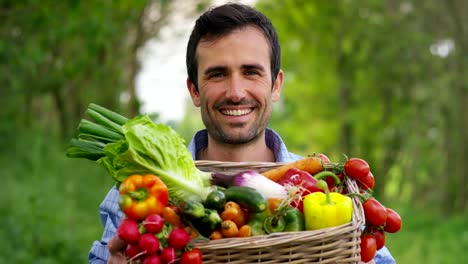 Portrait-of-a-happy-young-farmer-holding-fresh-vegetables-in-a-basket.-On-a-background-of-nature.