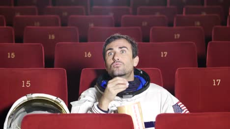 A-movie-astronaut-looks-at-a-movie-while-eating-pop-corn-and-enjoying-the-movie.-Concept-of:-cinema-and-space-films,-film-of-the-other-world,-surreal-situations.