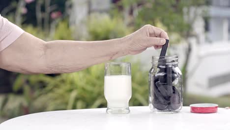 elderly-hand-dipping-and-stir-a-chocolate-cookie-In-milk-glass