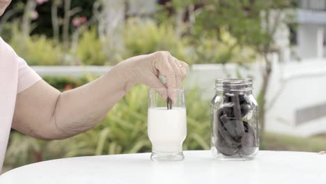 ältere-Menschen-hand-eintauchen-und-eine-Schoko-Cookie-In-Glas-Milch-rühren