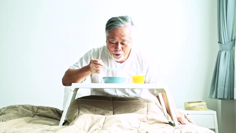 Älteren-Mann-im-Bett-gefrühstückt.-Alten-asiatischen-Mann-mit-weißem-Bart-Essen-Congee-und-Orangensaft.-Senior-home-Service-Konzept.