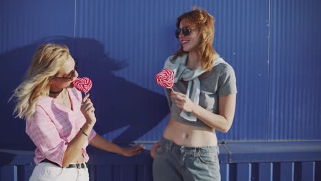 Two-young-attractive-women--walking--and-talking-on-street-and-eat-lollipop