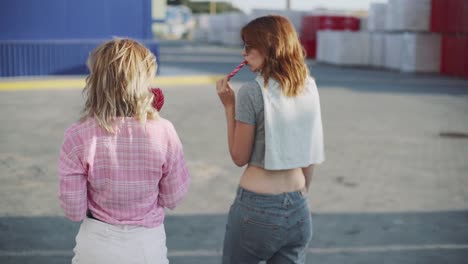 Two-young-attractive-women--walking--and-talking-on-street-and-eat-lollipop