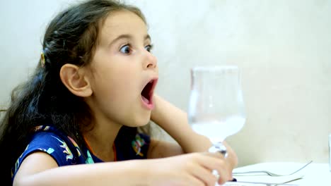 portrait,-close-up,-pretty-kid-girl,-curly-haired-brunette-wriggles-while-sitting-at-a-table-in-a-restaurant