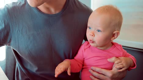 Otei-hermoso-sentado-en-la-cocina,-sosteniendo-a-su-hija-en-sus-brazos-y-su-papilla-de-alimentación.-Close-up