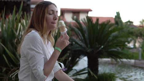 Retrato-de-hermosa-mujer-joven-positivo-comer-helado-en-el-fondo-de-las-palmeras