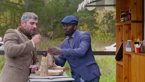 Two-speaking-men-eating-burgers-by-food-trailer