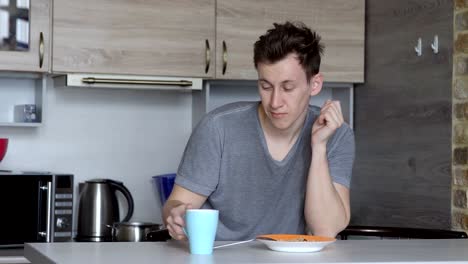 Young-sleepy-man-drinking-coffee-in-the-kitchen