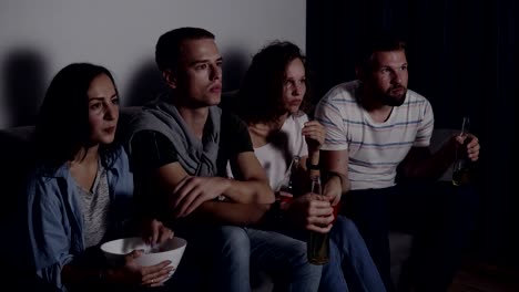 Four-friends-eating-popcorn,-drinking-beer-watch-horror-movie-together-and-are-very-captivated-and-scared,-sit-still.-Movie-night