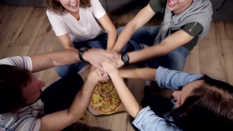 Top-view-of-young-people-taking-hand-to-hand-under-the-box-with-pizza-then-take-slices-of-hot-tasty-pizza-from-cardboard-box