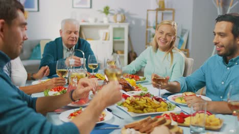 Große-Familie-und-Freunde-feiern-zu-Hause,-vielfältige-Gruppe-von-Menschen-versammelten-sich-am-Tisch-anstoßen-in-einem-Toast.-Leute-Essen,-trinken-und-Spaß-haben.-Tagsüber-Festlichkeit-im-Wohnzimmer.