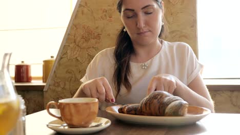 Hermosa-mujer-en-la-mesa-comiendo-un-croissant