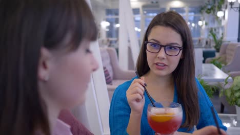 mujeres-alegres-amigos-de-gafas-comunican-y-beben-cócteles-a-través-de-paja-durante-el-almuerzo-en-la-cafetería-en-fin-de-semana