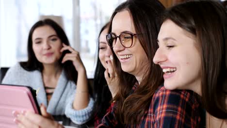 Cuatro-amigas-alegres-en-un-restaurante-a-comer-pizza,-beber-cerveza-y-ver-fotos-en-el-tablet.