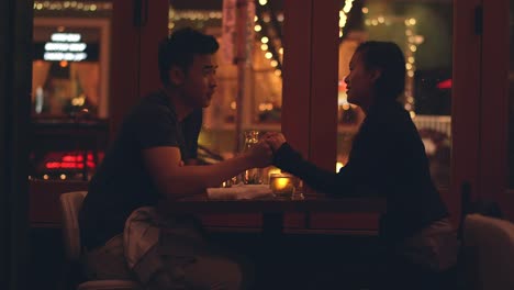 A-young-couple-laughing-on-a-romantic-dinner-date,-with-city-lights-behind-them