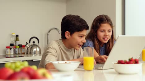 Linda-hermanos-usando-una-computadora-portátil-en-el-desayuno