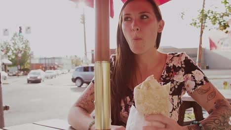 A-beautiful-girl-at-an-outdoor-table-eating-a-burrito,-slow-motion