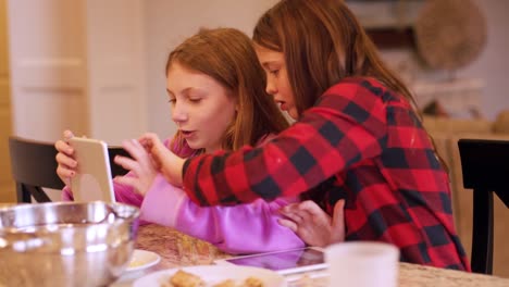 Two-friends-sitting-at-a-kitchen-island-using-their-tablets-and-eating-snacks