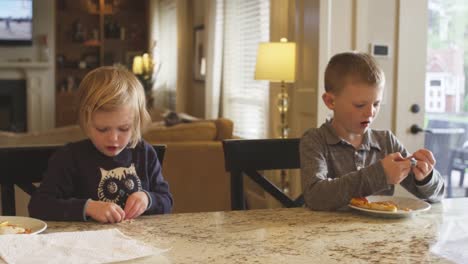 Hermano-y-hermana-comiendo-pizzas-caseras-en-el-mostrador-de-la-cocina