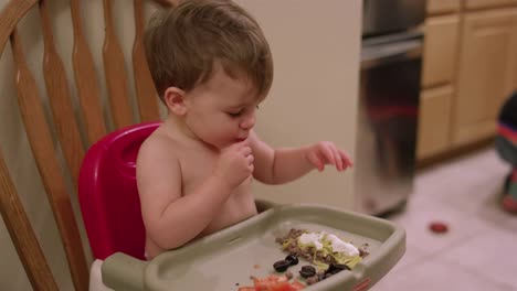 An-adorable-little-boy-in-a-high-chair-booster-seat-eating-taco-ingredients-with-his-hands