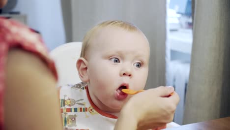 Madre-alimentando-al-bebé-con-cuchara-en-la-mesa-en-la-cocina-del-hogar