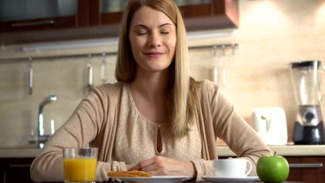 Hermoso-atractivo-casual-mujer-joven-sentada-en-su-cocina-sonriendo.-Feliz-y-relajada-en-casa