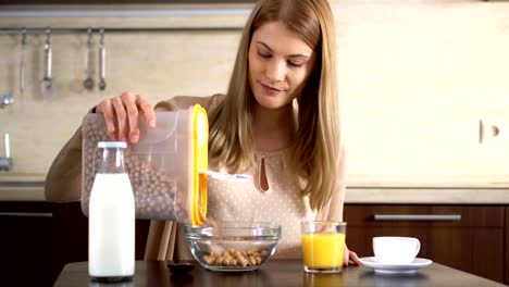 Schöne-junge-attraktive-Frau-Gießen-in-einer-Schüssel-Cornflakes-zum-Frühstück-in-der-Küche