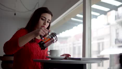 Woman-making-french-press-tea-at-breakfast.-Happy-smiling-girl-drinking-tea-in-cafe.-Caucasian-female-model.