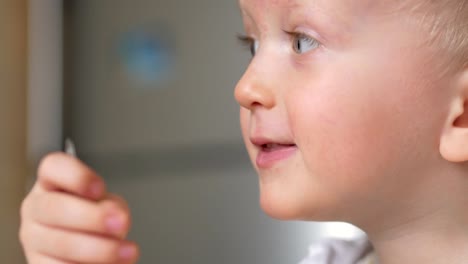 A-cute-blonde-boy-eats-a-porridge-with-a-spoon-from-a-plate-of-the-house.-Close-up