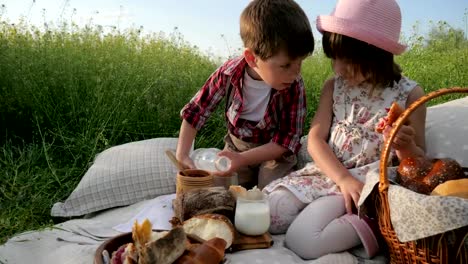 Children-at-picnic,-family-is-resting-in-nature,-kid-drinking-milk,-happy-girl-eating-bakery,-croissant,-brother-and-sister