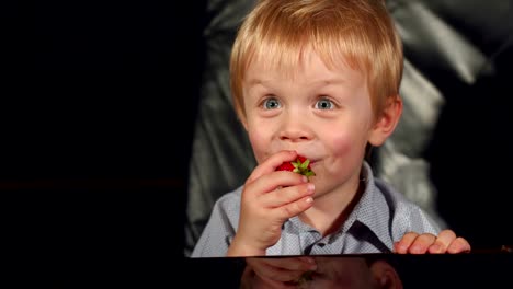 Little-boy-eating-strawberries-on-black-background