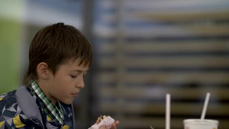 teenager-boy-eating-burger-sitting-in-cafe-in-city