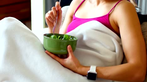 Woman-having-breakfast-on-sofa-in-living-room