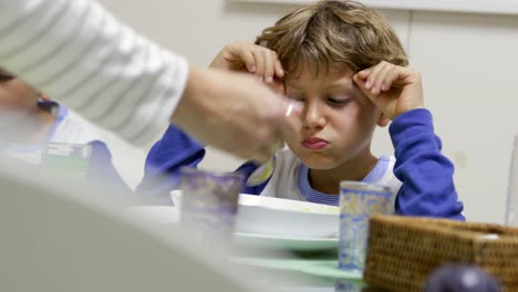 Casual-candid-moment-of-handsome-child-being-given-healthy-vegetable-soup-to-eat.-Mother-giving-young-boy-food-to-eat.-Child-eating-food-at-dinner-time-in-4K