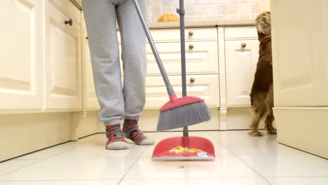 Hund-frisst-vom-Boden,-während-sein-Besitzer-den-Küchenboden-fegt
