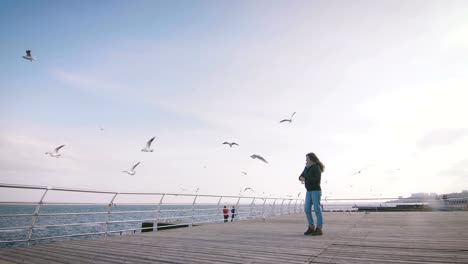 Young-woman-feeding-seagulls-at-winter-near-the-sea,-slow-motion