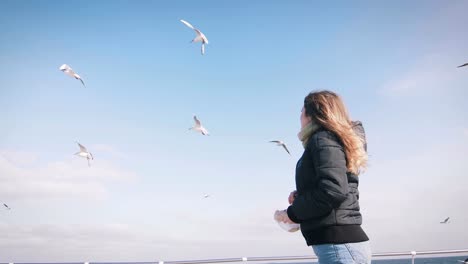 Young-woman-feeding-seagulls-at-winter-near-the-sea,-slow-motion