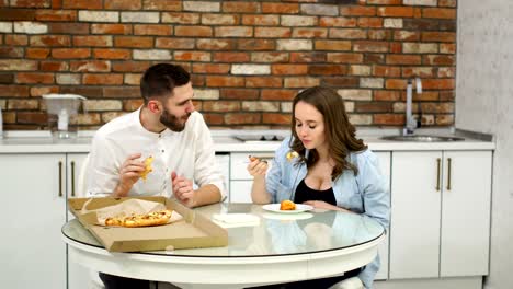 Man-and-pregnant-woman-eating-pizza-at-home-in-their-kitchen.-Poor-diet.-Fatty-foods.-Obesity