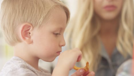 Young-loving-mother-gives-her-son-a-curly-frie-piece.-Her-son-dips-it-in-ketchup-and-eats-it-at-an-outdoor-food-court