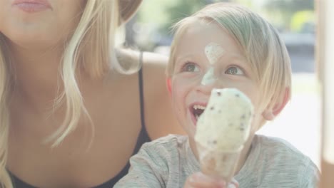 Little-kid-accidentally-shoves-an-ice-cream-cone-on-his-face,-and-laughs-out-loud-with-his-mother-at-the-park