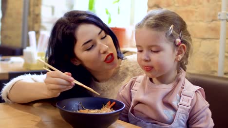 Coreana-joven-alimenta-a-su-hijita-con-fideos-en-el-restaurante