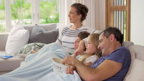 Zeit-mit-der-Familie-zu-Hause-kuscheln-auf-der-Couch-im-Wohnzimmer-mit-Popcorn-vor-dem-Fernseher