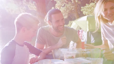 Family-Having-Picnic-As-They-Camp-By-Lake-On-Adventure-In-Forest