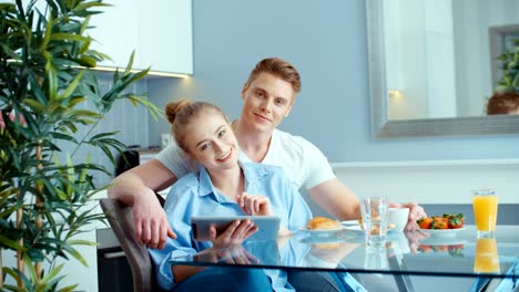 Pareja-joven-con-tableta-digital-desayunando-en-la-mesa-de-la-cocina.