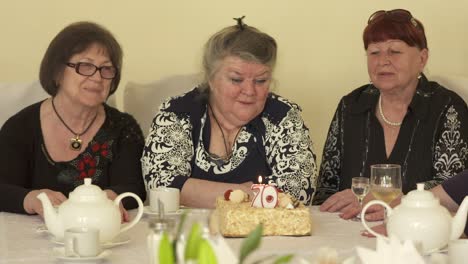 Senior-woman-with-female-friends-sitting-around-dinner-table-with-birthday-cake