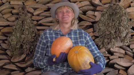 Happy-Woman-On-A-Background-Of-Stacked-Firewood-Holding-In-Her-Hand-Ripe-Pumpkin