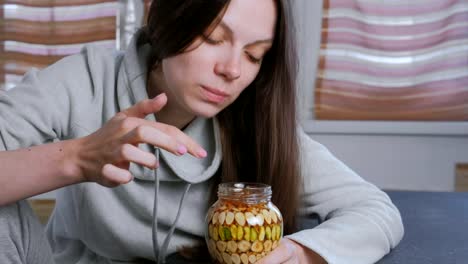 Woman-dips-her-finger-in-honey-with-nuts-in-the-jar.-Eats-honey-from-finger.